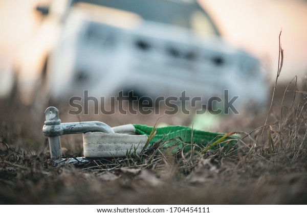 Tow rope with hook and blurred SUV car stuck in a\
swamp close up.