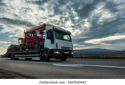 Tow truck or Flatbed truck towing two vehicles at dramatic sunset on a highway