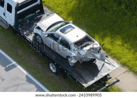 Tow truck hauling smashed vehicle on car accident site. Emergency services personnel responding to traffic crash on American street. First responders helping on road in the USA