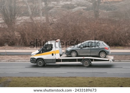 A tow truck helps a broken car on the highway. The car has been damaged by a collision and needs to be repaired