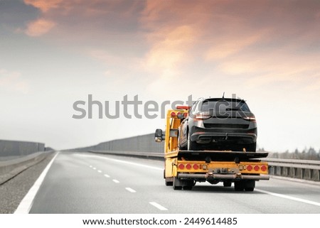 A tow truck helps a broken car on the highway. The car has been damaged by a collision and needs to be repaired