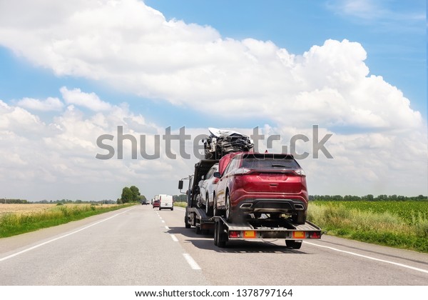 Tow truck trailer on highway carrying\
three damaged cars sold on insurance car auctions for repair and\
recovery.  Vehicles shipment and rescue\
service