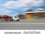 A tow truck is transporting a car. Side view of a moving tow truck transporting a car on a platform against a blurred background.