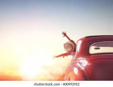 Toward adventure! Girl relaxing and enjoying road trip. Happy girl rides into the sunset in vintage car.