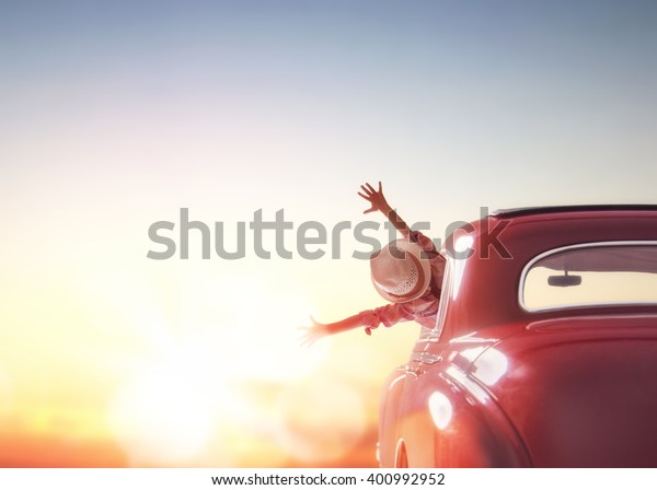 Toward adventure! Girl\
relaxing and enjoying road trip. Happy girl rides into the sunset\
in vintage car.