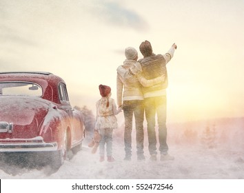 Toward Adventure! Happy Family Relaxing And Enjoying Road Trip. Mom, Dad, Child And Vintage Car On Snowy Winter Nature Background. Christmas Holidays Time.