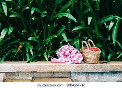 Towel And Basket With Swimming And Sunbath Accesories On The Stone Ledge By The Pool In The Tropics. Nobody