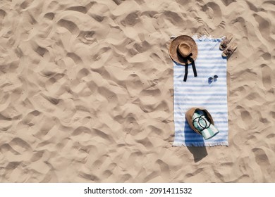 Towel with beach accessories on sand, top view. Space for text