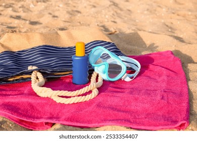 Towel with snorkeling mask, beach bag and bottle of sunscreen cream on sand, closeup - Powered by Shutterstock