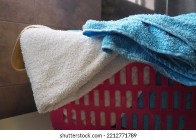 Towels In The Laundry Basket. Blue And Pink Cotton Terry Towels Are Thrown Into A Pink Plastic Basket. Housekeeping. Storing And Separating Laundry Before Washing. Light From Above From An Open Window