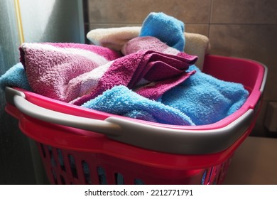 Towels In The Laundry Basket. Blue And Pink Cotton Terry Towels Are Thrown Into A Pink Plastic Basket. Housekeeping. Storing And Separating Laundry Before Washing. Light From Above From An Open Window