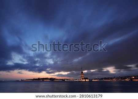 Maiden’s Tower at blue hour beneath dramatic clouds with long exposure water and illuminated Istanbul shoreline.