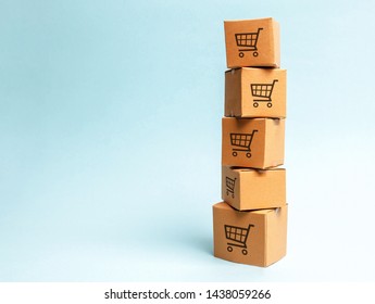 Tower Of Cardboard Boxes With Pattern Of Shopping Carts On A Blue Background. Commerce, Online Shopping. Purchasing Power, Delivery Order. E-commerce, Logistics, Distribution And Sales.