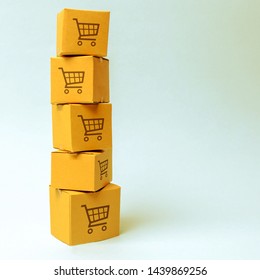 Tower Of Cardboard Boxes With Pattern Of Shopping Carts On A Blue Background. Commerce, Online Shopping. E-commerce, Logistics, Distribution And Sales. Purchasing Power, Delivery Order.