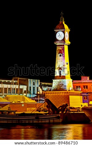 Tower of the Clock, built in 1772, at fishermen pier at night time, seen from Maremagnum, Barcelona, Spain