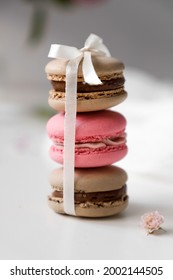 tower of colourful french macarons with a bow of ribbon, pink and brown dessert cake stands in a row on the white background close up, useful sweets