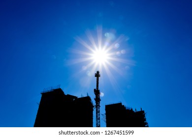 Tower crane under construction between the two high-rise buildings against the blue sky and sun. The industrial look.