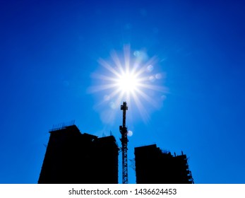 Tower crane under construction between the two high-rise buildings against the blue sky and sun. The industrial look.