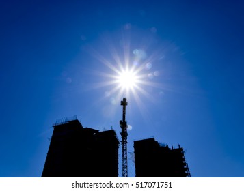 Tower crane under construction between the two high-rise buildings against the blue sky and sun. The industrial look.