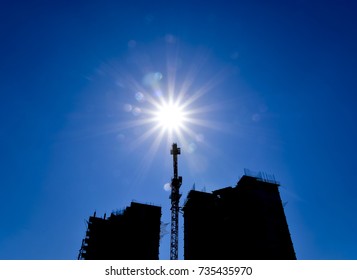 Tower crane under construction between the two high-rise buildings against the blue sky and sun. The industrial look.