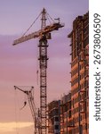 Tower cranes are working on constructing a new residential apartment building against a beautiful sunset sky, showcasing urban development and progress