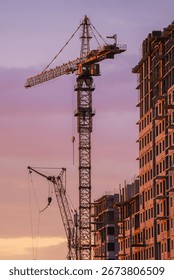 Tower cranes are working on constructing a new residential apartment building against a beautiful sunset sky, showcasing urban development and progress
