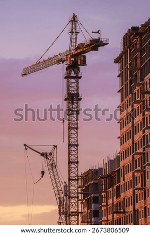 Tower cranes are working on constructing a new residential apartment building against a beautiful sunset sky, showcasing urban development and progress