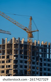 Tower cranes are working on the construction site of a new residential building, lifting heavy materials against a backdrop of a clear blue sky