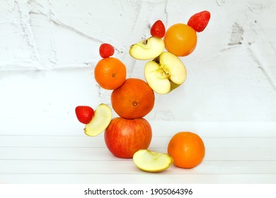 A tower of fruits - apples, tangerines, strawberries on a white background. Fruit composition balancing food.  Healthy food concept. Fruits stacked vertically.