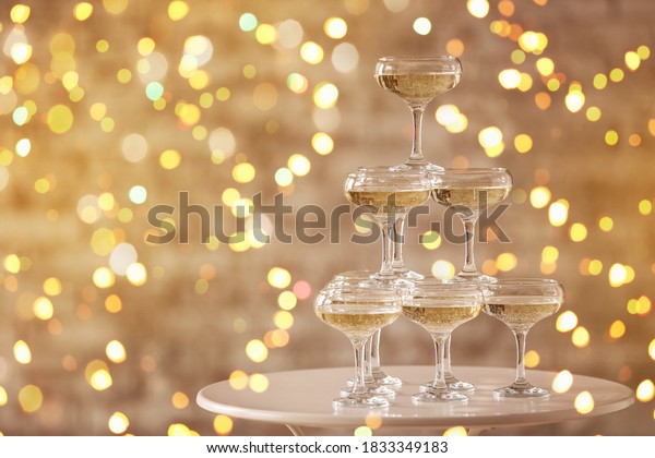 Tower made of glasses with champagne on table\
against blurred lights