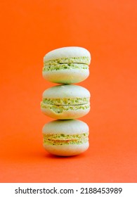tower of mint green pastel macarons close-up on bright orange background, Stack of three pistachio or green tea cookies. Vertical