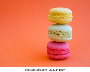 tower of multi-colored assorted bright macarons close-up, on orange background, Stack of three yellow, green and pink cookies. Copy spase, side view