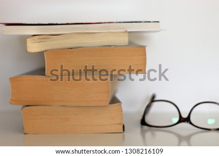 Tower of old books and glasses on white table over white background.