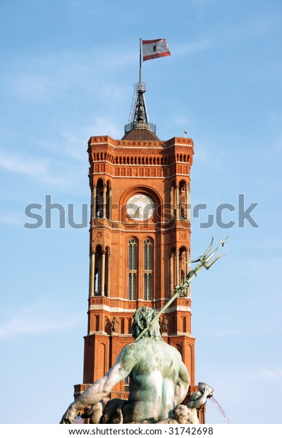 Tower of Rathaus the\
Berlin Town Hall made of red bricks with town flag and detail of\
the Neptune fountain.