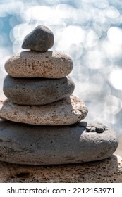 A Tower Of Stones. Balanced Pyramid Of Pebbles On The Beach On A Sunny Day. Blue Sea In The Background. Selective Focus, Bokeh. Zen Stones On The Sea Beach, Meditation, Spa, Harmony, Tranquility