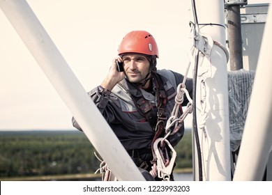 Tower Technician Talking On A Cell Phone On A Telecommunications Tower. The Concept Of Checking Cellular Signal. Copy Space For Your Text