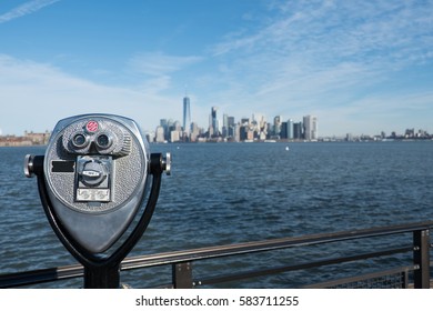 Tower viewer telescope looking at lower Manhattan skyline from Liberty Island. Railing and binoculars on a stand for tourists to view New York City from across the New York Harbor.