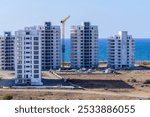 Towering buildings rise amidst a sandy shoreline and glistening waters, highlighting the blend of nature and urban architecture under a clear sky.