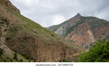 a towering cliff face with visible stratification, towering over a lush green forest under a gloomy overcast sky. - Powered by Shutterstock