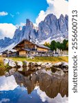 Towering Dolomite peaks, a charming wooden chalet reflects beautifully in a serene alpine lake, Geisleralm Dolomites Val Di Funes in Italy Adolf Munkel Trail in Puez Odle Nature Park