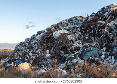A towering heap of mixed refuse extends towards the horizon, illustrating mans impact on nature with plastic, clothing, and organic waste.