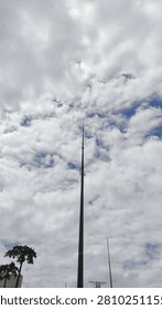 A towering lightning rod pierces a dramatic, cloudy sky streaked with deep blue. A minimalist, vertical shot from a low angle shows the contrast between the man-made structure and nature.