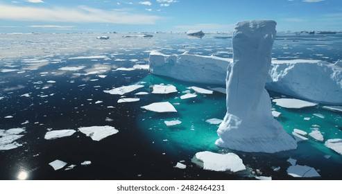 Towering melting iceberg in Arctic icy ocean. Snow covered glacier drift under blue sunny sky. Pure ice floats in turquoise water. Ecology, melting ice, climate change global warming. Aerial view - Powered by Shutterstock