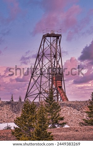 A towering old mining structure amidst pine trees under a stunning sunset sky, depicting the remnants of Colorado's heart land and its rich history in nature and mountains