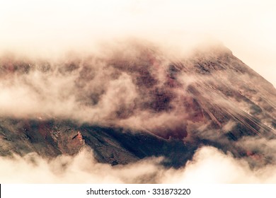 A towering volcano releases billowing smoke and dust, causing destruction as it blankets the majestic mountains in a dark cloud. - Powered by Shutterstock