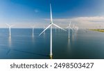 Towering wind turbines gracefully spin offshore, harnessing the power of the wind to produce clean energy against a vibrant sky. drone top view at a windmill park in the ocean