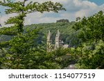 Towers of the Church of Saints Cosmas and Damien, seen from a hill with abundant vegetation and lush green trees, sunny spring day in Clervaux, Luxembourg