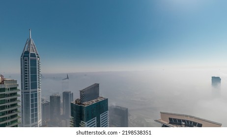 Towers covered by rare early morning winter fog above the Dubai Marina skyline with sun going up and skyscrapers rooftops aerial timelapse. Top view from above clouds. Dubai, UAE - Powered by Shutterstock