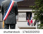 A town hall and the French flag with the mayor in front.