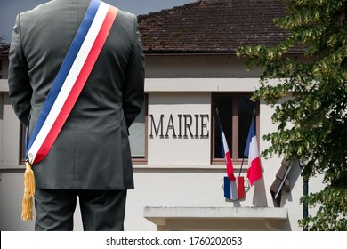 A Town Hall And The French Flag With The Mayor In Front.